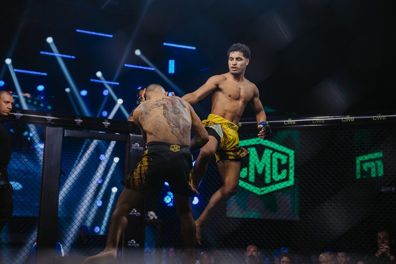Atletas trocando golpes em pé encostados na grade do cage da LMC